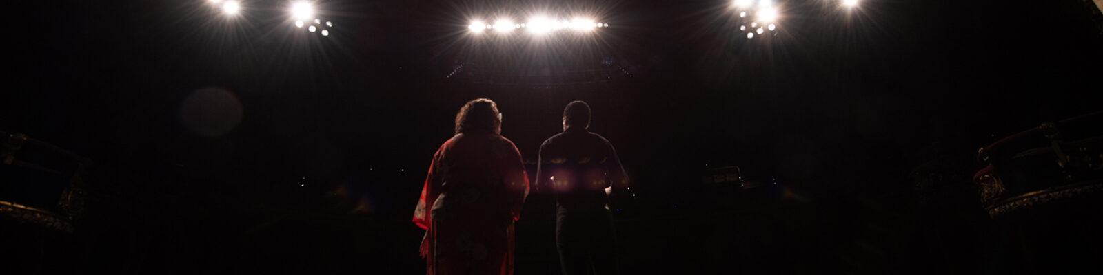 Two students standing on a dark stage beneath multiple spotlights