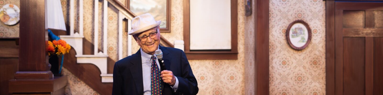 Norman Lear stands onstage, holding a microphone.